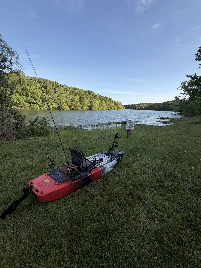 Red modular fishing kayak rigged with a rod and trolling motor at a canoe and kayak launch on Lake Jacomo, Missouri